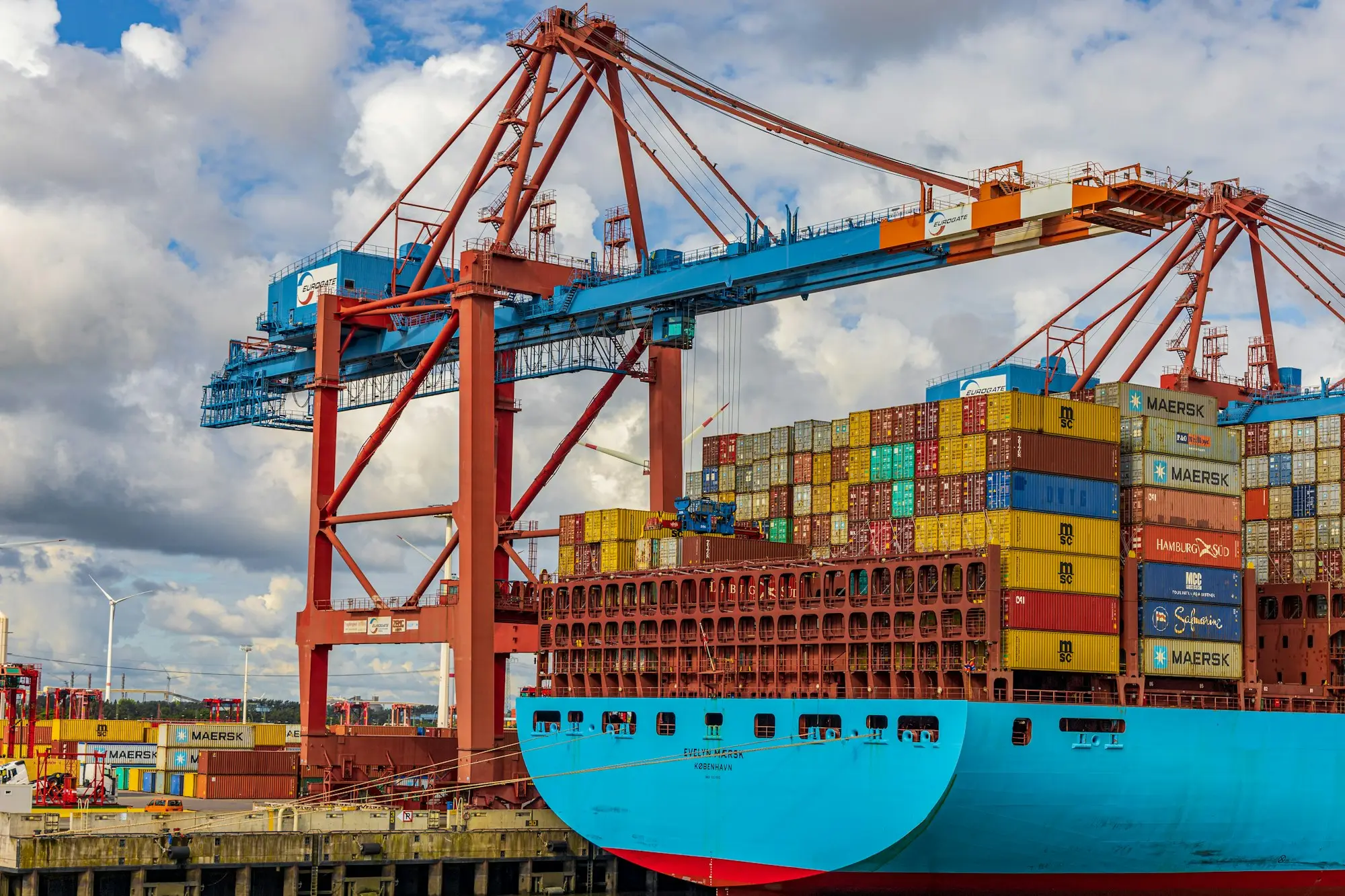 Container ship being loaded under a gantry crane, with stacked containers bound for export
